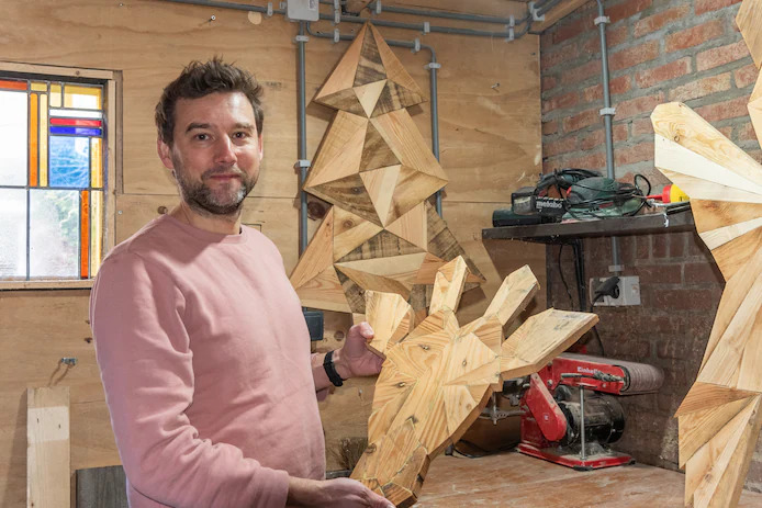 Man houdt handgemaakte geometrische giraffe kop wanddecoratie van resthout vast in werkplaats